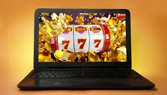 A laptop on a yellow background with slot symbols on the screen