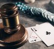 An image of a judge’s gavel on a table with playing cards and chips