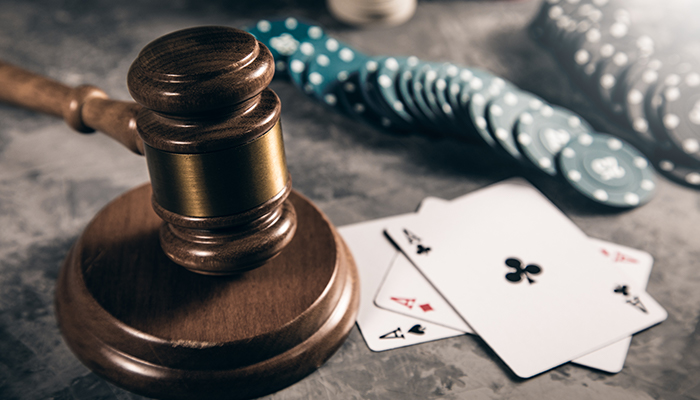 An image of a judge’s gavel on a table with playing cards and chips